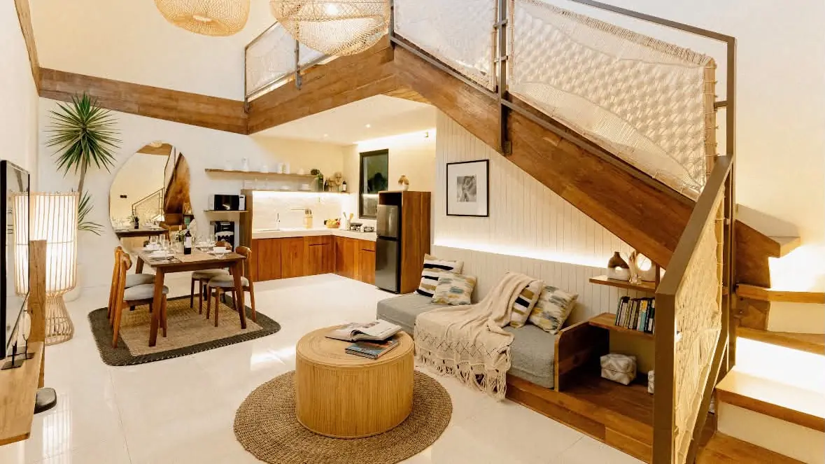 Double-height living room with a timber staircase, rattan lights and a sofa nook in a furnished Seminyak villa