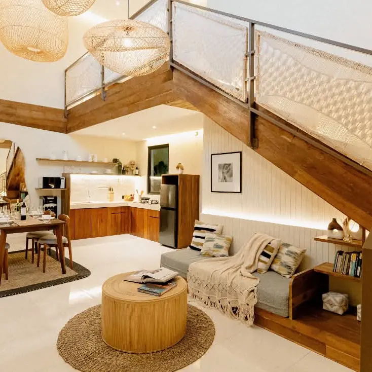 Double-height living room with a timber staircase, rattan lights and a sofa nook in a furnished Seminyak villa